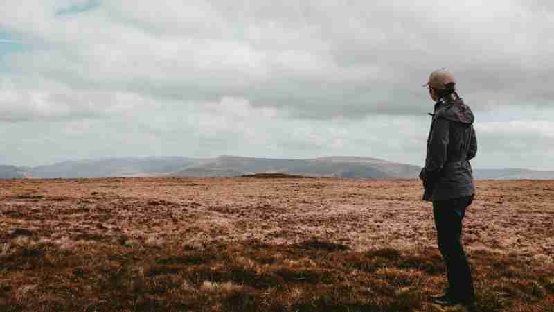 A person stands in a vast, open landscape with mountains under a cloudy sky., tags: landwirtschaft - pexel
